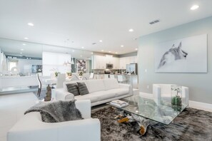 Un salon moderne avec un canapé blanc, une table basse en verre et un grand tableau abstrait accroché au mur.