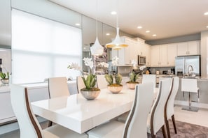 Une cuisine moderne avec des meubles blancs, un îlot central doté de chaises et des luminaires suspendus.