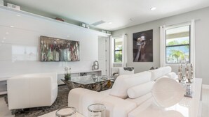 A modern living room with a white sofa, a glass coffee table, and artwork on the walls. - Beautiful Villa With Private Pool, Close to Disney, Orlando Villa 2942 (Kissimmee)