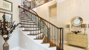 A staircase with wooden steps and black metal railings, a vase with flowers, a decorative mirror, and a gold-toned dresser. - Rent a Luxury Villa on Reunion Resort, Minutes From Disney, Orlando Villa 3539 (Kissimmee)