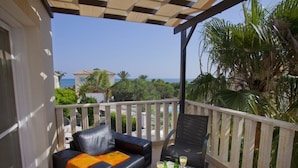 A balcony with a black leather sofa and a table, overlooking a coastal area with palm trees and a view of the sea. - Cyprus Villa Near the Beach, Sotira Villa 1001 (Sotira)