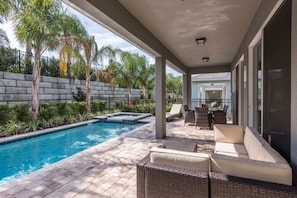 A covered outdoor swimming pool area with a hot tub, wicker furniture, and a stone wall. - Villa in Encore Resort at Reunion 3438 (Kissimmee)