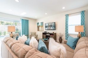 A living room with a beige sofa, teal curtains, and a flat-screen TV on the wall. - Villa in Encore Resort at Reunion 3438 (Kissimmee)