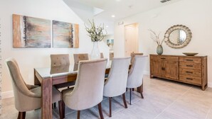 A dining area with a wooden table and chairs, a wooden cabinet, and two abstract paintings on the wall. - Villa in Encore Resort at Reunion 3438 (Kissimmee)
