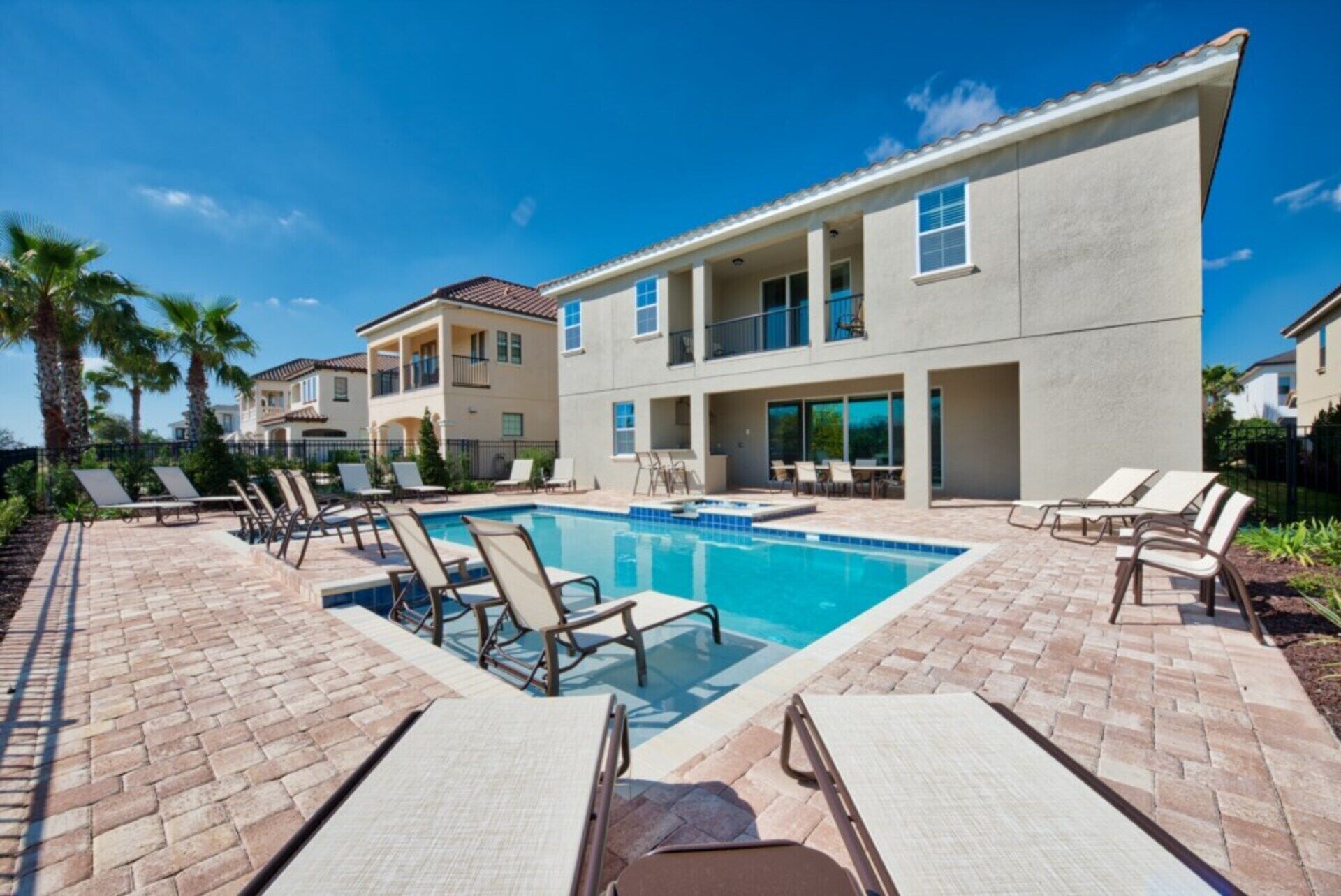 A modern residential building with a swimming pool, lounge chairs, and palm trees.