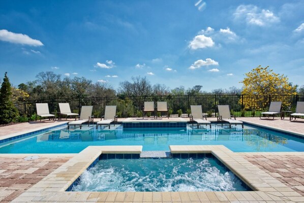 Ein rechteckiger Pool mit einem Whirlpool in der Mitte, umgeben von Liegestühlen und einem Zaun.