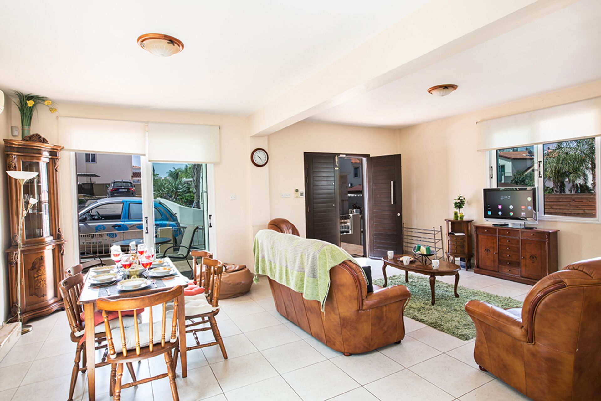 A spacious living area with a dining table, leather sofas, a television, and a clock on the wall.