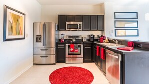 A modern kitchen with stainless steel appliances, black cabinets, and a red rug.