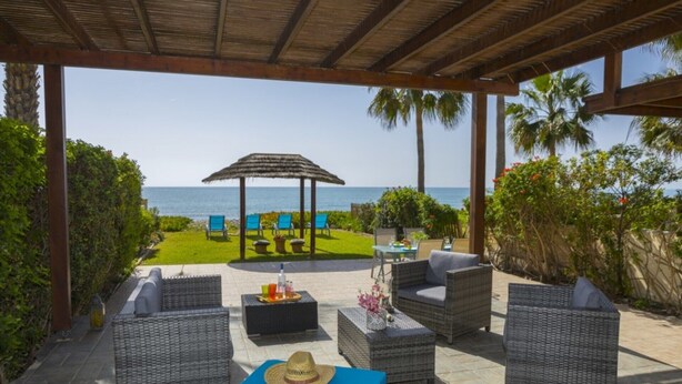 Une terrasse extérieure avec des meubles en osier, une table avec des boissons et une vue sur la mer.