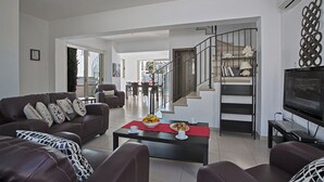 Ein geräumiger Wohnbereich mit einer Sofagarnitur, einem Couchtisch mit Früchten, einer Treppe und einem Fernseher.