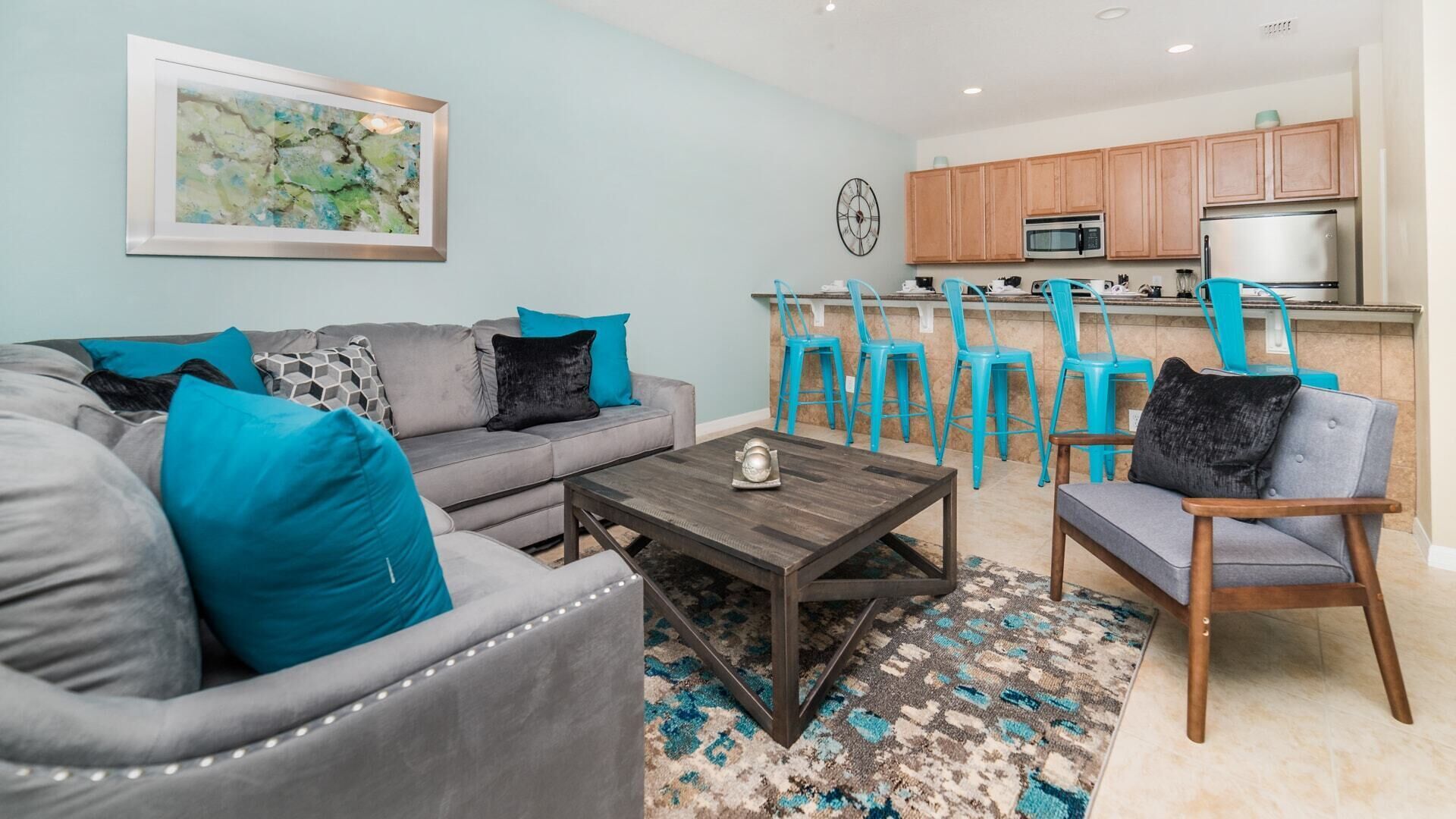 A living room with a grey sofa, teal cushions, a wooden coffee table, and a patterned rug.