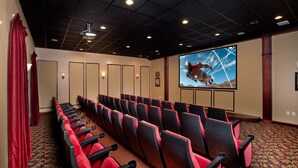 A theater with rows of red and black seats, a large screen, and a ceiling with recessed lighting.
