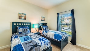 A bedroom with two beds, each with Star Wars themed bedding, a window with blinds, and two paintings on the wall.