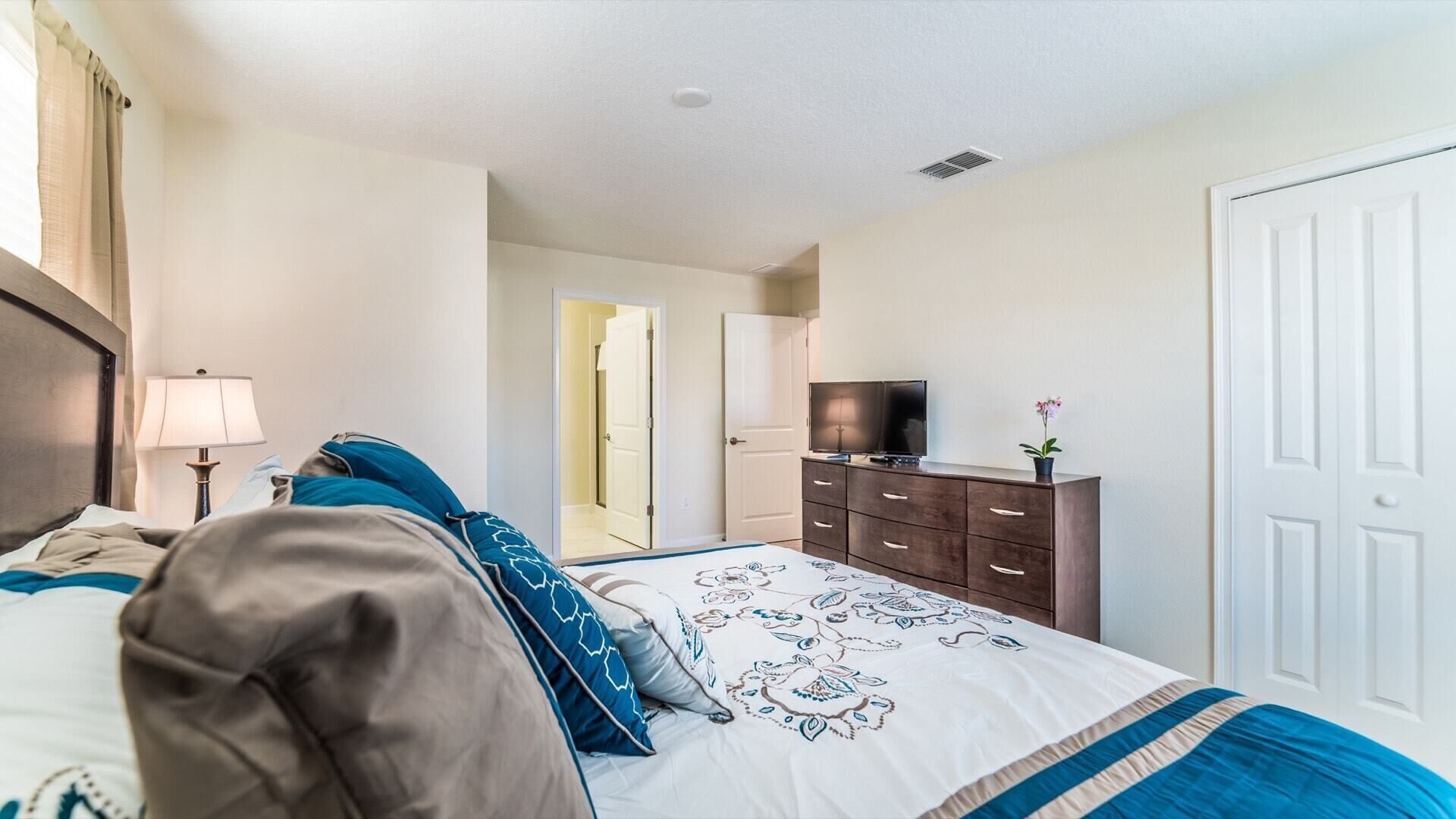 A hotel room with a bed, a dresser, a television, and a door.