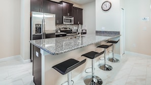A modern kitchen with dark wood cabinets, stainless steel appliances, a granite countertop, and three bar stools.