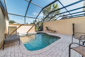An outdoor swimming pool with a glass enclosure, surrounded by lounge chairs and a paved deck. - Luxury 3 Bedroom House on Windsor Hills Resort, Orlando House 1902 (Kissimmee)