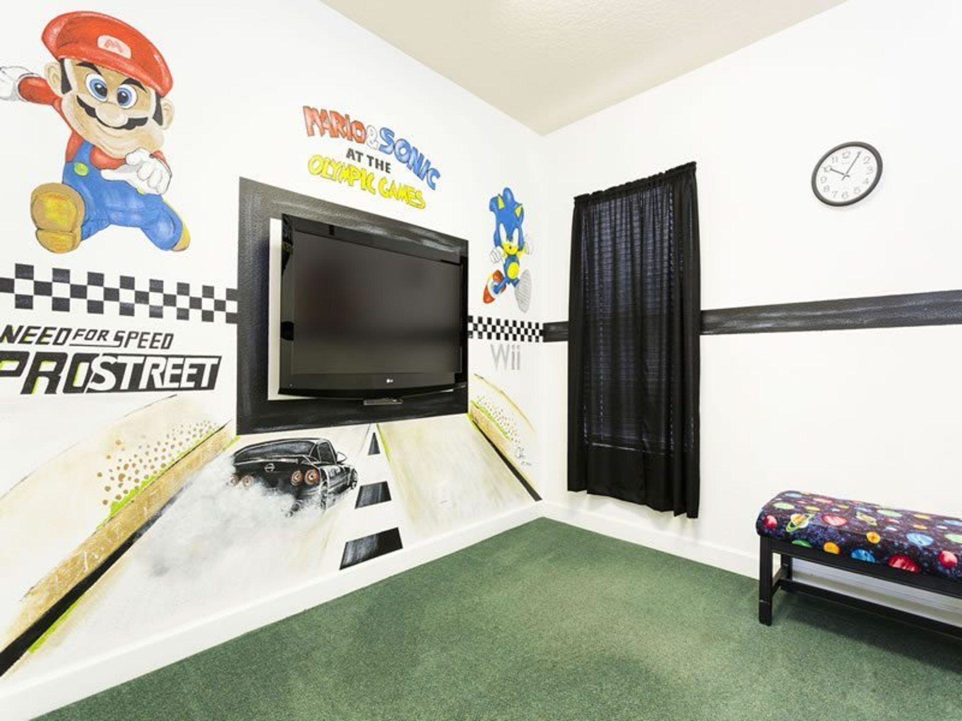 A room with a large TV, a Nintendo Wii console, and a racing-themed wall.