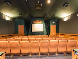 Um cinema com fileiras de assentos laranja, uma tela grande e um projetor.