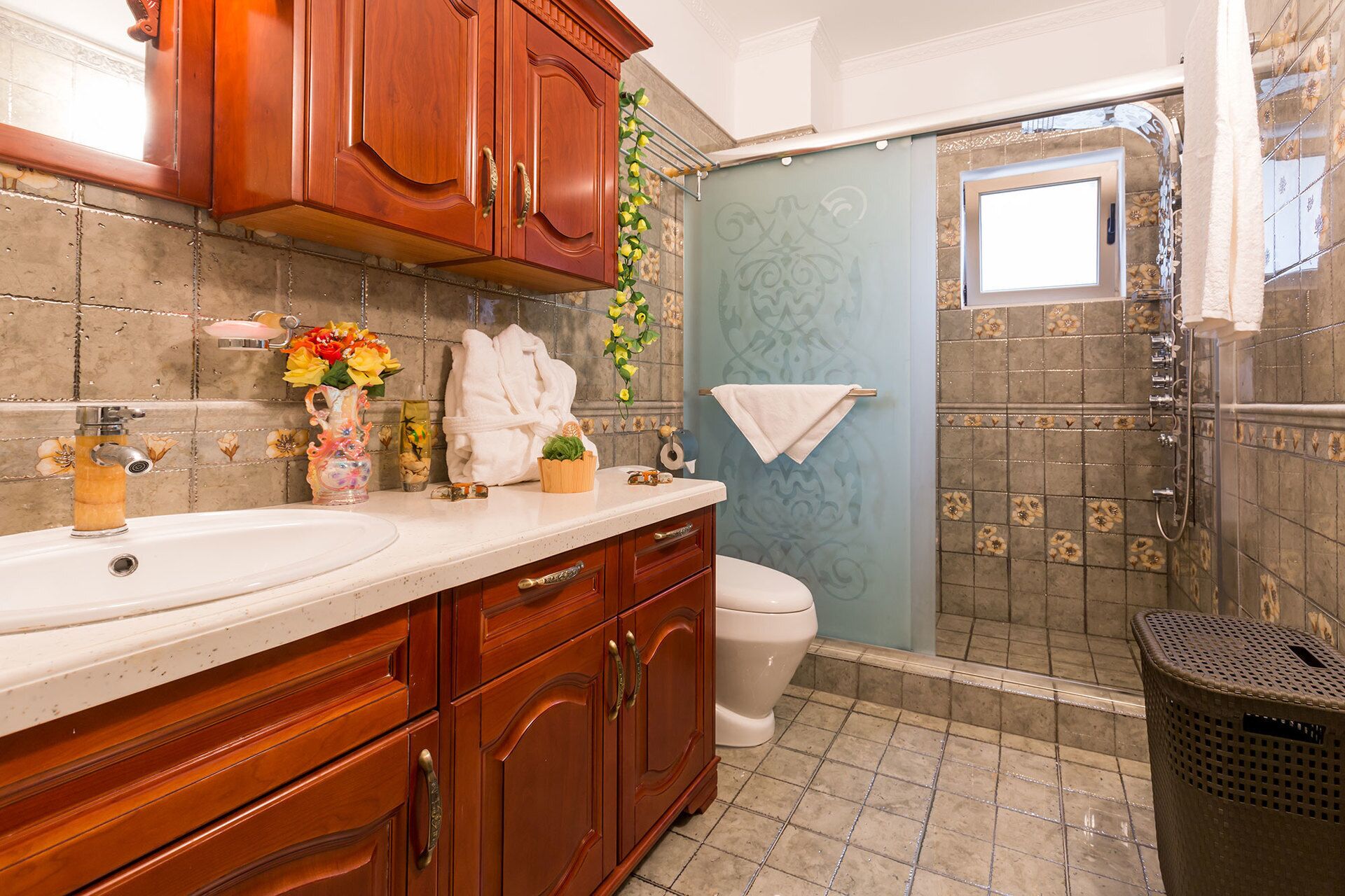 A bathroom with wooden cabinets, a sink, a toilet, and a shower area.