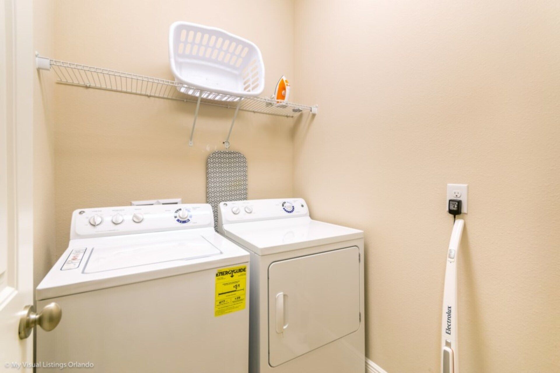 A laundry room with two white washers and dryers, a drying rack, and a wall-mounted iron.