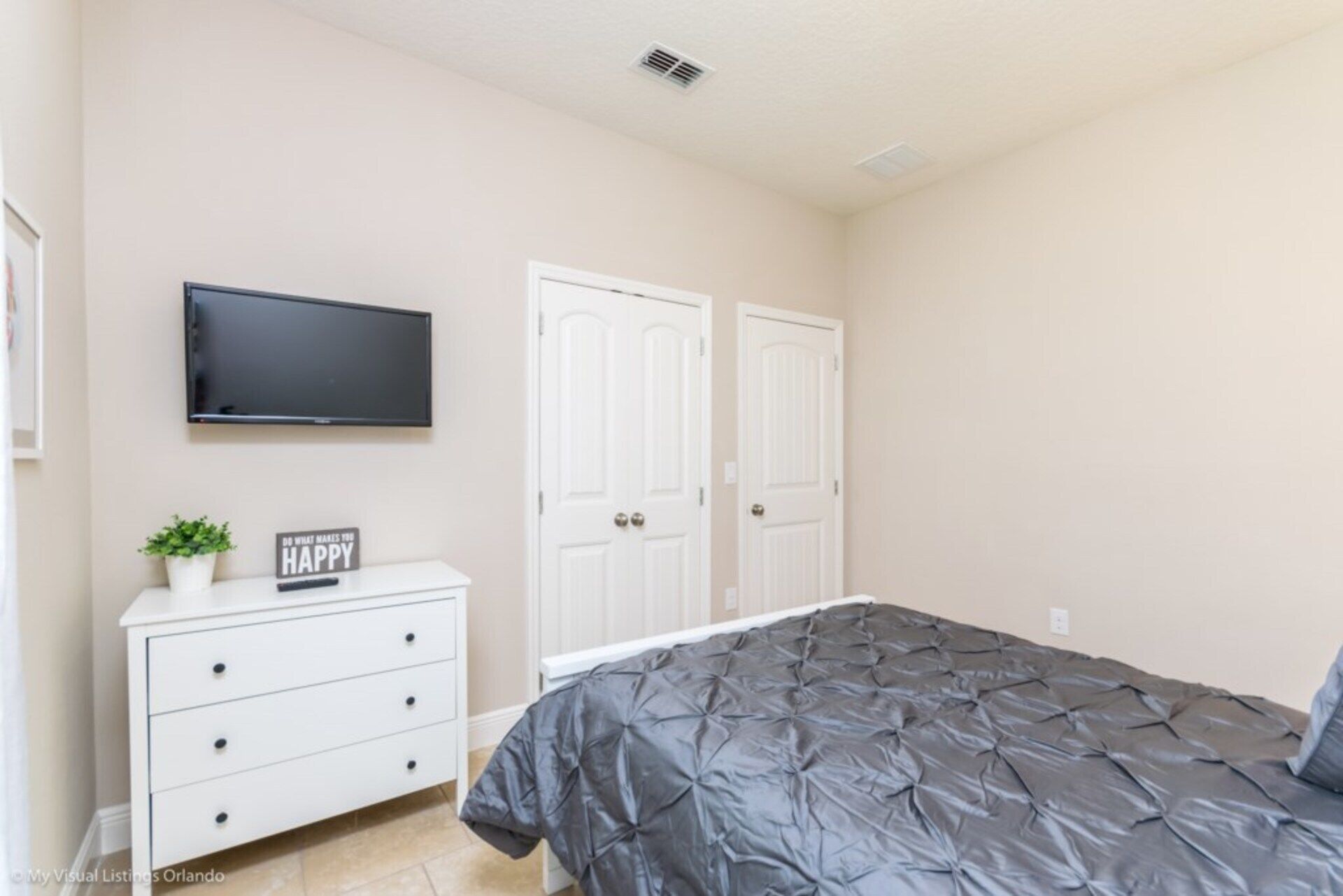 A bedroom with a bed, a TV mounted on the wall, a dresser, and two doors.