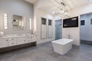 A modern bathroom with a large vanity, a freestanding bathtub, and a mirror with lights.