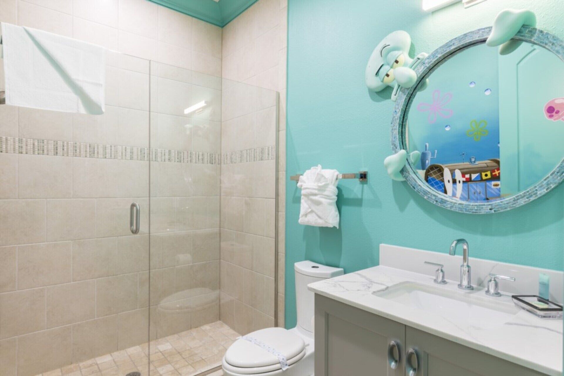 A bathroom with a shower, toilet, sink, and a mirror with a decorative frame.