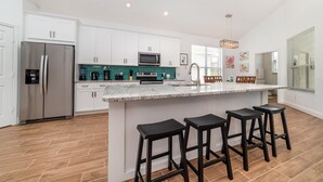 A modern kitchen with white cabinets, a stainless steel refrigerator, a microwave, and a large island with bar stools. - Luxury 5 Bedroom Villa on Windsor Palms Resort, Orlando Villa 3310 (Kissimmee)