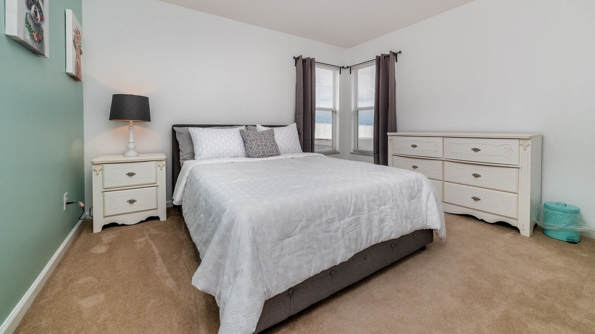 A bedroom with a bed, nightstands, a dresser, and a window with curtains.