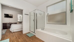 Ein modernes Badezimmer mit Duschkabine aus Glas, einer großen Badewanne und einem Fenster mit Jalousien.