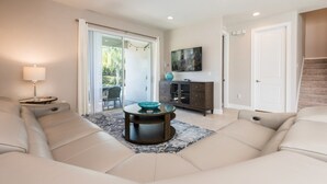 A modern living room with a beige sofa, a glass coffee table, a dark wooden cabinet, and a television on the wall. - Luxury 8 Bedroom Villa on Encore Resort at Reunion, Orlando Villa 1987 (Kissimmee)