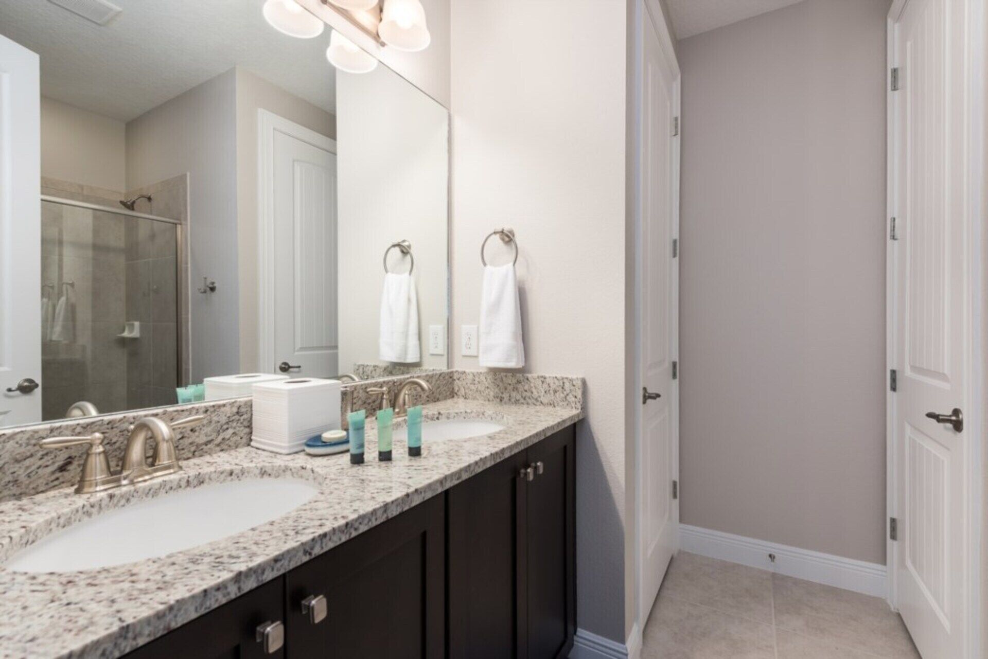 A bathroom with two sinks, dark cabinets, a large mirror, and a shower area.