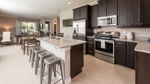 A modern kitchen with dark cabinets, stainless steel appliances, and a central island with bar stools. - Luxury 8 Bedroom Villa on Encore Resort at Reunion, Orlando Villa 1987 (Kissimmee)