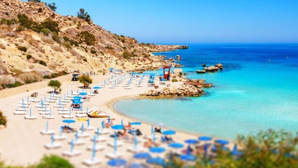 Une plage avec des chaises longues et des parasols, un terrain rocheux et une eau d’un bleu limpide.