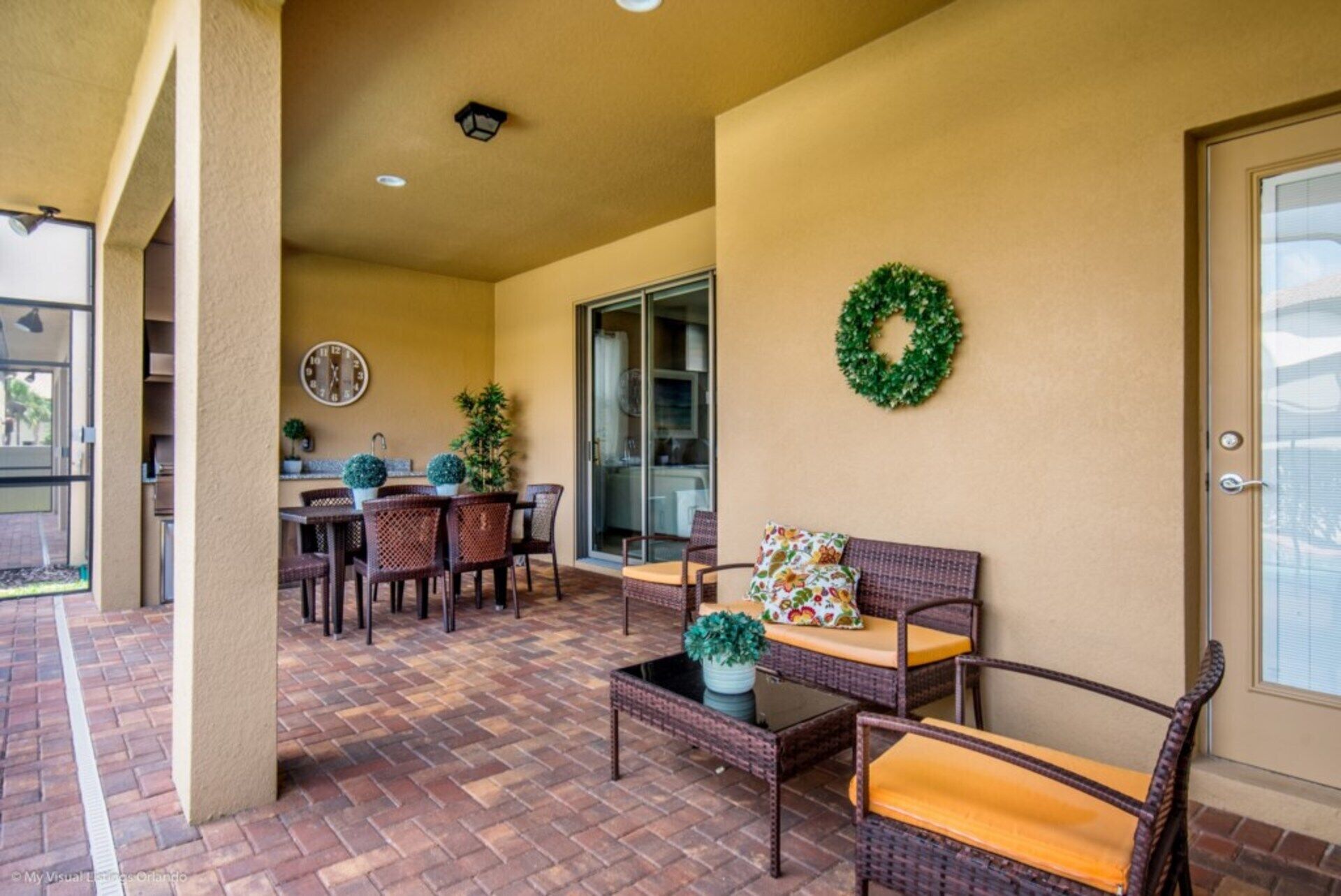 A covered patio area with wicker furniture, a clock, and a wreath on the wall.