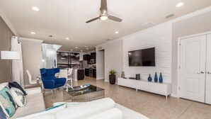 A modern living room with a white sofa, blue chairs, a coffee table, and a TV mounted on a textured wall. - Beautiful Villa With Private Pool, Close to Disney, Orlando Villa 2641 (Kissimmee)