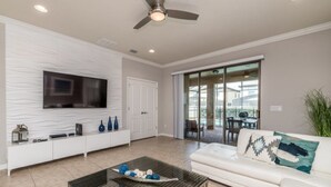 A modern living room with a flat-screen TV, a white sofa, a coffee table, and a sliding glass door leading to an outdoor area. - Beautiful Villa With Private Pool, Close to Disney, Orlando Villa 2641 (Kissimmee)