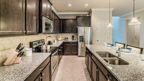 A modern kitchen with dark wood cabinets, granite countertops, stainless steel appliances, and pendant lighting. - Beautiful Villa With Private Pool, Close to Disney, Orlando Villa 1266 (Kissimmee)