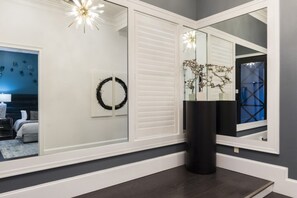 Interior moderno com piso de madeira escura, um espelho grande refletindo um quarto com parede azul e planta decorativa.