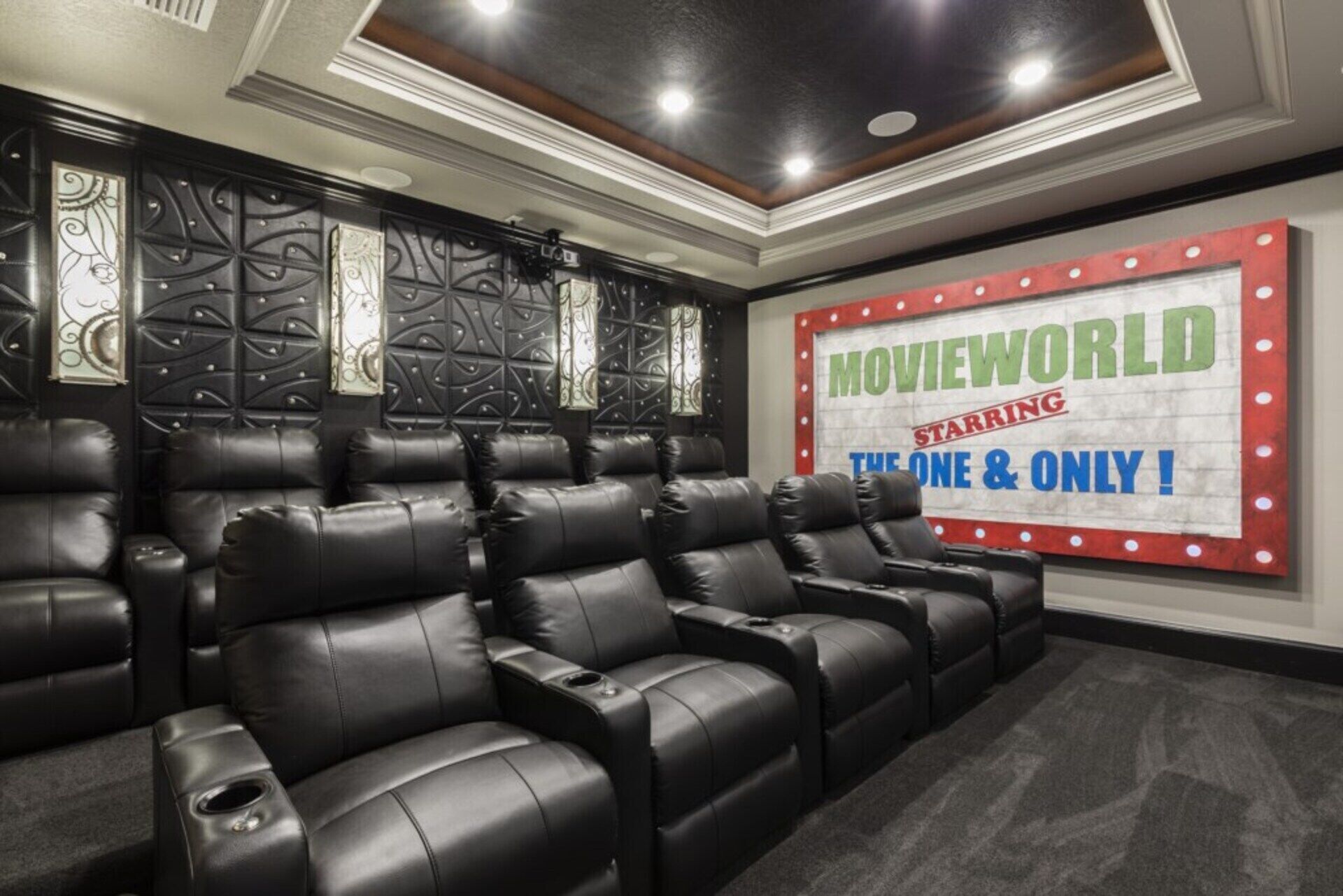 Un cine en casa con sillones reclinables de cuero negro, un panel decorativo y un letrero que dice 'MOVIEWORLD'.