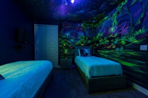 A bedroom with two beds, a door, and a mural of a forest scene.