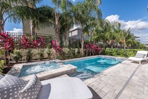 A swimming pool with a hot tub, surrounded by palm trees and tropical plants.
