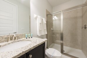 A bathroom with a granite countertop, a white toilet, a glass shower enclosure, and a mirror with a towel rack.