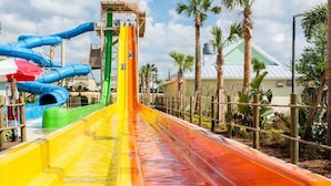 Ein Wasserpark mit zahlreichen Rutschen in verschiedenen Farben, umgeben von Palmen und einem klaren Himmel.