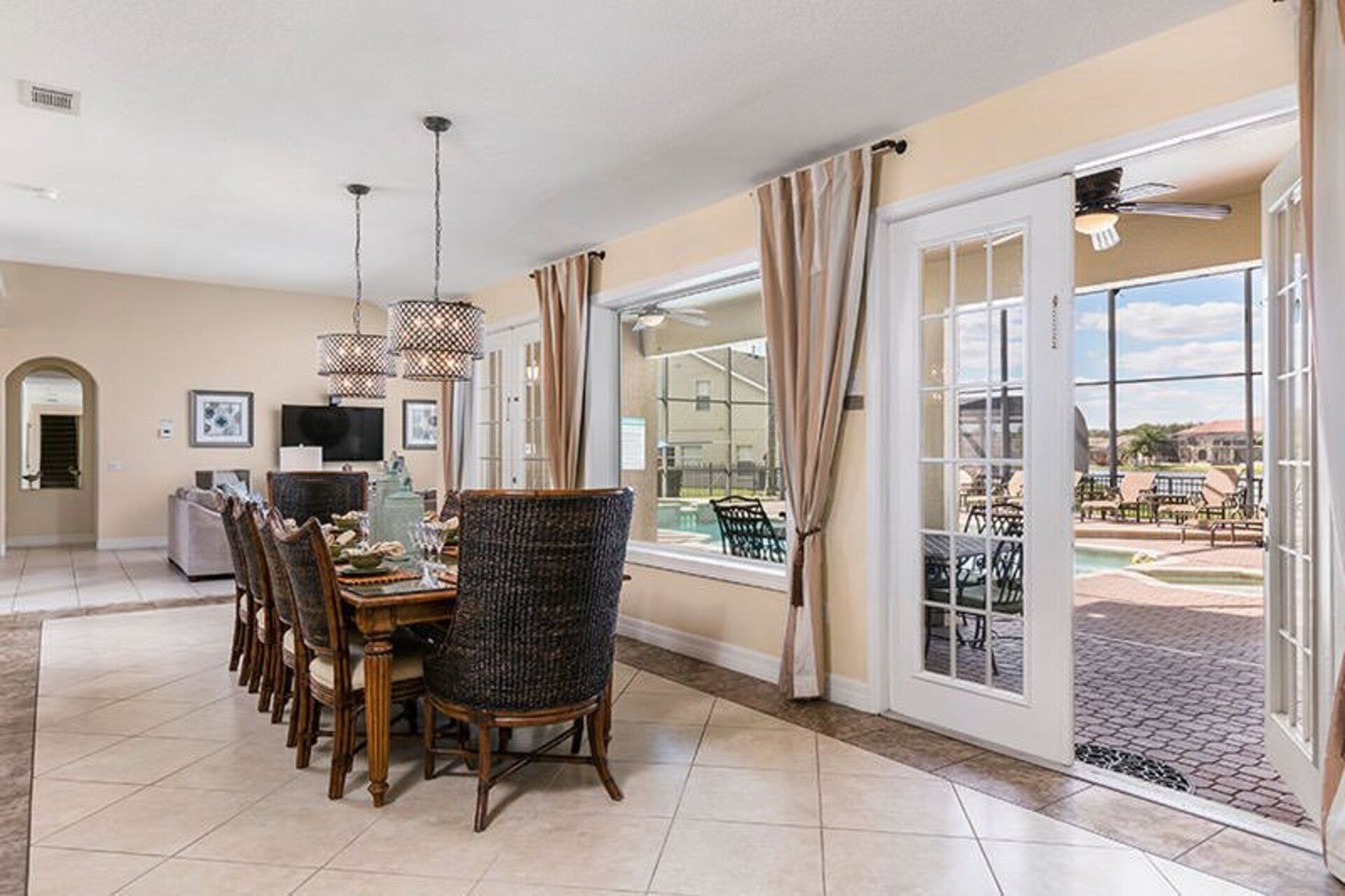 A dining area with a table set for six, a television, and a view of a pool and outdoor seating.
