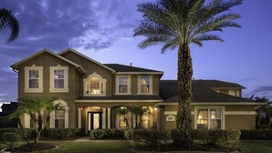 A two-story house with a symmetrical facade, a central entrance with a covered porch, and a large palm tree in the front yard. - Luxury 9 Bedroom Villa on Osceola County, Orlando Villa 3569 (Kissimmee)