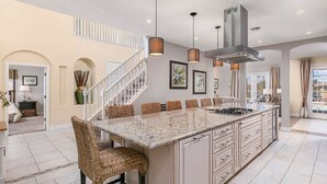 A spacious kitchen with a large island, modern pendant lighting, and a staircase leading to an upper level. - Luxury 9 Bedroom Villa on Osceola County, Orlando Villa 3569 (Kissimmee)