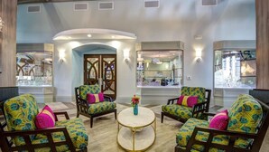 A spacious lobby with a central round table, surrounded by four armchairs with floral upholstery and pink cushions.