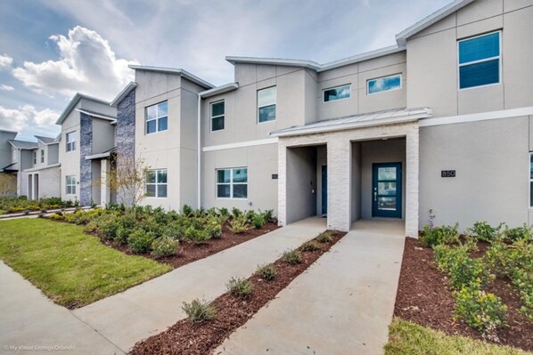 A modern apartment building with a flat roof, large windows, and a well-maintained lawn.
