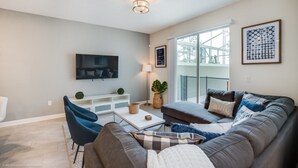 Moderni olohuone, jossa on harmaa sohva, sohvapöytä ja seinälle asennettu televisio.